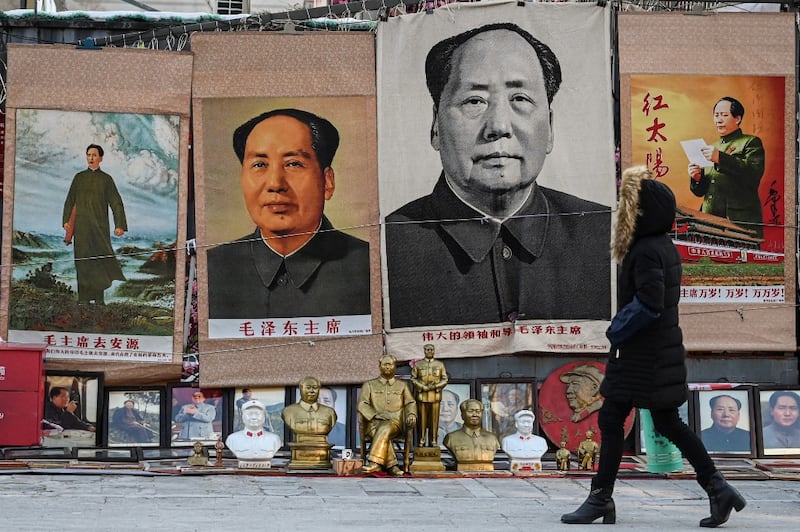 A woman walks past posters of the late Chinese Communist leader Mao Zedong at a stall in an antique market in Beijing, Dec. 26, 2023.